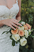 Braut mit Ehering hält Strauß aus cremefarbenen und pfirsichfarbenen Rosen