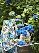 Blauer Gartenstuhl mit Hortensien (Hydrangea) und floralem Tuch