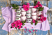 Tassen in Rosa und mit Blumen auf kariertem Tuch arrangiert