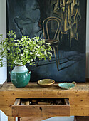 Still life with painting and ceramic plates, vase and flowers on rustic wooden table