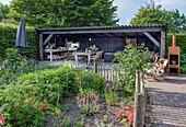 Gartenlaube mit Holztisch und Stühlen, umgeben von blühenden Stauden