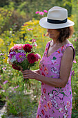 Woman with straw hat and bouquet of dahlias (Dahlia), roses (Rosa), autumn anemones (Anemone Hupehensis) and wild carrot