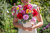 Frau trägt Vase mit buntem Strauß aus Dahlien (Dahlia), orientalischen Knöteriche (Persicaria orientalis), Bartblume (Caryopteris), und Borretsch