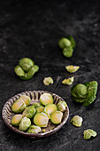 Whole and halved Brussels sprouts in a bowl on a dark background