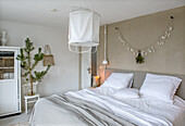 Bedroom in neutral tones with decorative plant, garland and white bed linen with grey bedspread