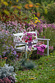 Bunter Strauss aus Dahlien (Dahlia), Rosen (Rosa), Astern (Aster) auf Bank vor bunten Blumenbeeten im herbstlichen Garten