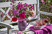 Bunter Strauss aus Dahlien (Dahlia), Rosen (Rosa), Astern (Aster) auf Bank im herbstlichen Garten