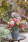 Strauß aus Rosen (Rosa), Schneebeeren (Symphoricarpos)  und Wildem Wein in Vase auf der Terrasse