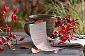 Note with handwritten poem about autumn leaves, with linen napkin, cup and rose hips, still life