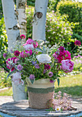 Bunter Strauß aus Pfingstrosen (Paeonia), Scheinwaldmeister, Skabiose, Wollziest, Katzenminze, Giersch und Zierlauch in Vase auf Gartentisch