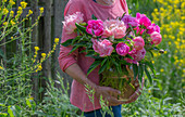 Frau mit Strauß aus Pfingstrosen (Paeonia) im Garten