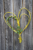 DIY heart made of yellow branches and ivy on wooden wall