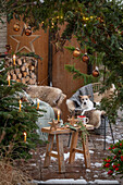 Weihnachtlich rustikal geschmückte Terrasse mit Sitzplatz vor Thuje und Christbaum mit Anhängern