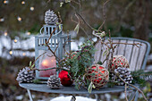 Laterne auf Gartentisch mit Kieferzapfen, Christbaumkugeln, Haselzweigen