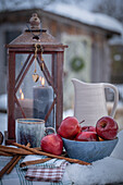 Laterne mit Keramik Krug, Tasse, Äpfel, Zimtstangen in winterlichem Garten