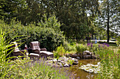 Sitting area with rattan armchairs next to pond in summer garden