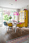 Dining room with yellow chairs, pink pendant light and yellow display cabinet