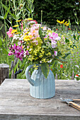 Colourful summer flowers in a blue ceramic vase on a wooden table in the garden