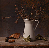 White enamel pot with dried branches and autumnal finds on a wooden background