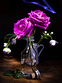 Bottiglia di vetro con due rose fucsia e tulipani doppi tardivi su fondo nero con lampo blu su un piano di legno con tappo e foglie.