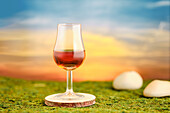 Glass of whisky on mossy ground with sunset in the background