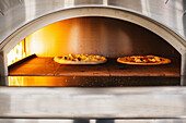 Two pizzas in the burning pizza oven