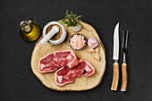 Raw lamb chops with spices and cutlery on wooden board