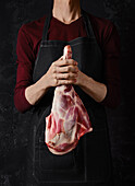 Butcher holds raw leg of lamb in his hands