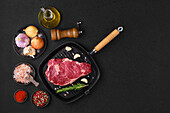 Rohes Ribeye-Steak in Gusseisenpfanne mit Gewürzen und Olivenöl