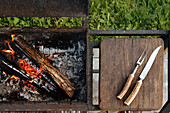 Ready for the barbecue: Burning wood and cutlery on a chopping board