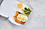 Breakfast box with fried egg, sausage, potato wedges and gherkins