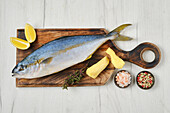 Whole raw yellowtail king mackerel with lemon, ginger and spices on wooden board