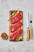 Raw beef steaks on wooden board with spices and cutlery