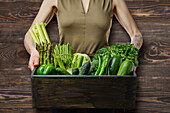 Woman holding box of fresh green vegetables