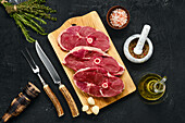 Raw lamb steaks with spices and cutlery on a wooden board
