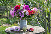 Strauß aus Dahlie (Dahlia), Flammenblume (Phlox), Riesendost, Fenchel, Prachtspiere (Astilbe), Zierlauch im Krug auf Gartentisch neben Obst