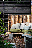 Seating area in the garden with wooden benches, cushions and privacy screen