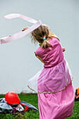Kind im Prinzessinnenkleid tanzt mit Schwungband im Garten