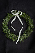 Tied rosemary wreath (Rosmarinus officinalis) with white lace loop on black background