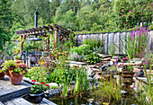 Üppiger Garten mit Pergola und Teich im Sommer