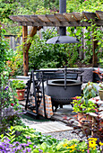 Fire pit under pergola in lush garden with potted plants