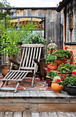 Gemütliche Terrasse mit Holzliege, Geranien und Topfpflanzen