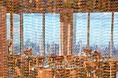 Blick durch einen sechseckigen gemusterten Vorhang auf den Essbereich eines Restaurants mit einer Stadtlandschaft mit dem Empire State Building im Hintergrund