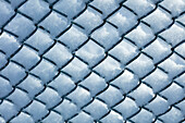 Snow on chain link fence against blue sky