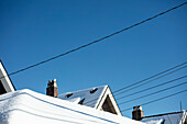 Schneebedeckte Dächer und elektrische Leitungen vor blauem Himmel