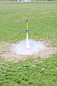 Blue and yellow toy rocket taking off from a white circular launch pad