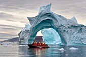 Grönland, Nordwestküste, Inglefield Fjord in Richtung Qaanaaq, Eisberg, der einen Bogen bildet, und ein Erkundungszodiac des Hurtigruten-Kreuzfahrtschiffs MS Fram