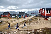 Grönland, Nordwestküste, Qaanaaq oder New Thule, Inuit-Kinder laufen zu ihrer Lehrerin, im Hintergrund ein Eisberg