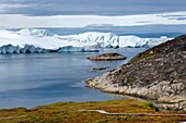 Grönland, Westküste, Diskobucht, Ilulissat, von der UNESCO zum Weltnaturerbe erklärter Eisfjord an der Mündung des Sermeq-Kujalleq-Gletschers (Jakobshavn-Gletscher), Wanderung auf dem Holzsteg zur Sermermiut-Stätte und Fischerboot am Fuße der Eisberge
