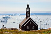 Grönland, Westküste, Diskobucht, Ilulissat, Zionskirche aus dem späten 18. Jahrhundert und Eisberge im Hintergrund